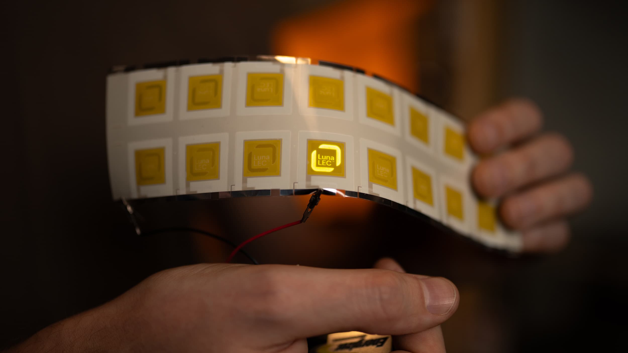 Flexible LEC tile band glowing yellow, held in hand
